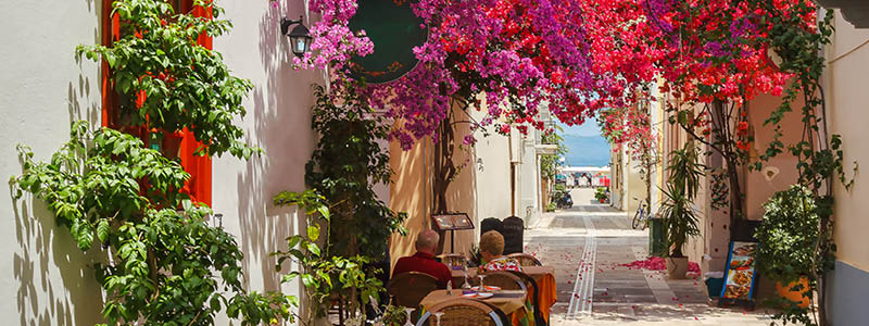 Mysigt grekiskt cafe under rosa och rda blommor i Nafplio, Grekland.